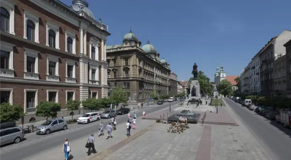 Kraków: pomnik Grunwaldzki, zabytkowe budynki i spacerujący ludzie. Wśród nich można sobie wyobrazić znane osoby z Krakowa.