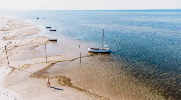 Spokojna plaża w Kuźnicy, gdzie kilka łodzi czeka na wodzie, a samotna postać spaceruje brzegiem.