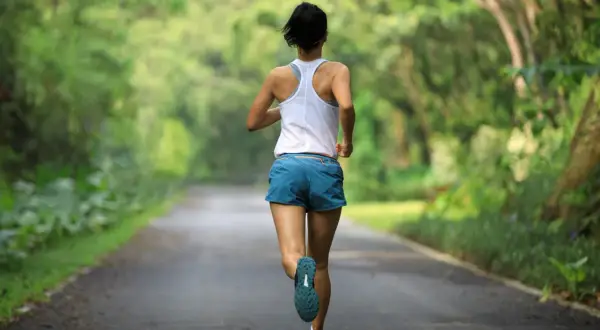 Kobieta biegnie leśną drogą. Czy bieganie to cardio? Zdecydowanie tak! To świetny trening dla serca.