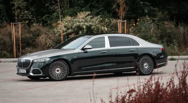 Elegancki Mercedes-Maybach S680 w ciemnozielonym kolorze z dwukolorowym nadwoziem, zaparkowany na tle zieleni.
