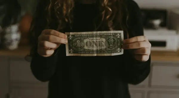 Dłoń trzyma banknot jednodolarowy, symbolizujący początek budowania majątku.