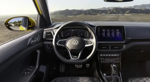 Interni di un'auto Volkswagen con volante, cruscotto digitale e schermo touchscreen. Vista dal posto di guida verso l'esterno.