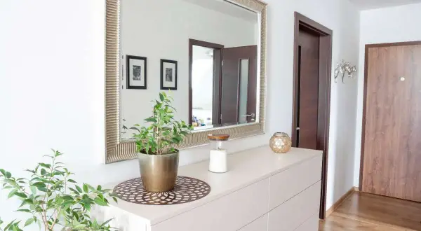 Soluzioni idee piccolo ingresso casa: specchio decorativo, cassettiera chiara, pianta verde e candela creano un'atmosfera accogliente.