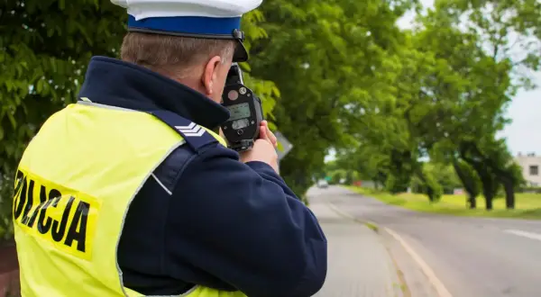 Policjant w kamizelce odblaskowej mierzy prędkość samochodu za pomocą fotoradaru.