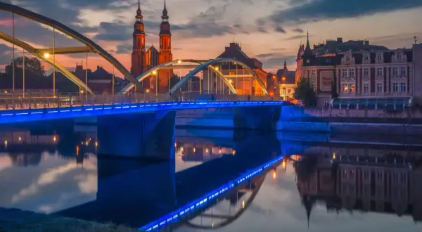 Zachód słońca nad Odrą, most z niebieskim podświetleniem i katedra w tle. Odkryj magiczne miejsca opolskie.