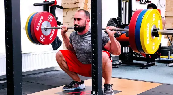 Man utför en djup knäböj med skivstång, en klassisk övning som en del av sin russian squat routine.