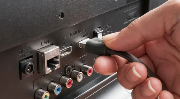 Dłoń podłącza kabel do portu HDMI ARC w telewizorze, obok złącza LAN.