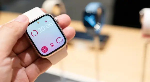 Une main tient une montre connectée affichant l'heure 20:06, des indicateurs d'activité et le logo watchOS 26.