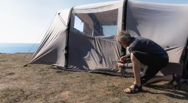 Mężczyzna rozbija namiot na trawiastym klifie nad morzem. Czy można rozbić namiot na plaży? To miejsce wygląda idealnie.
