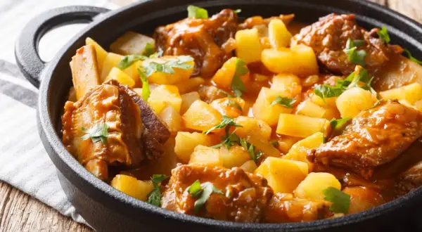 Un reconfortante guiso de patatas con costillas, cubierto de perejil fresco, servido en una olla de hierro fundido.