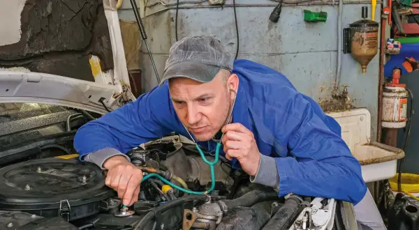 Mechanik z wyspecjalizowanym stetoskopem nasłuchuje pracy silnika, sprawdzając, czy tłoki działają prawidłowo.