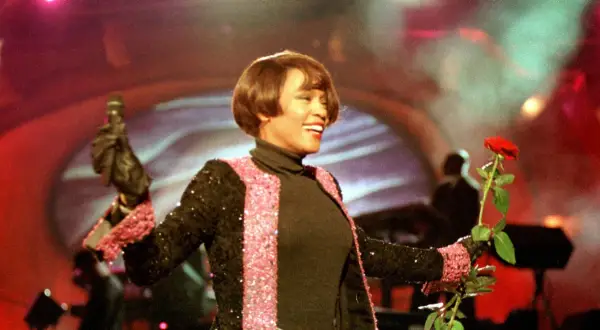 Whitney Houston w Polsce, z mikrofonem i czerwoną różą, w błyszczącej marynarce.