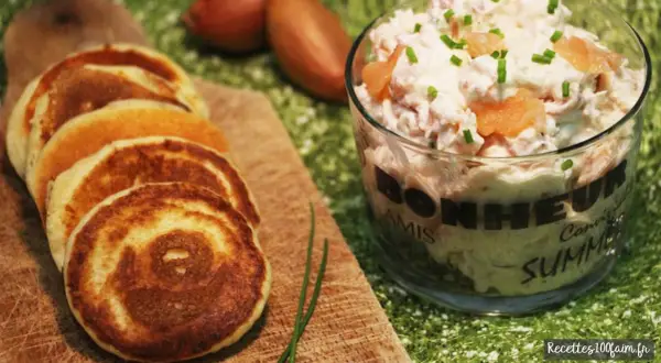 Petits blinis dorés accompagnant un délicieux verre de rillettes de saumon, parsemé de ciboulette fraîche.