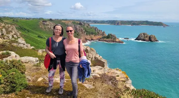 Zwei Frauen genießen den Ausblick auf die Kanalinseln. Tolle kanalinseln urlaub erfahrungen mit türkisfarbenem Meer und Felsen.