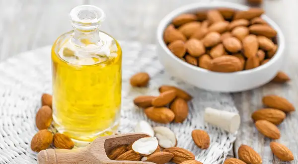 Aceite de almendras en botella, almendras en cuenco y esparcidas. El aceite de almendras mancha la piel con el sol, ¡pero nutre!