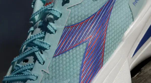Jasnoniebieskie buty sportowe Diadora Olympia z niebieskimi i pomarańczowymi paskami, idealne na bieżnię.