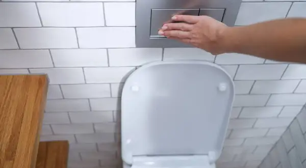 Mano presionando el botón de descarga de los tipos de cisternas wc empotradas.