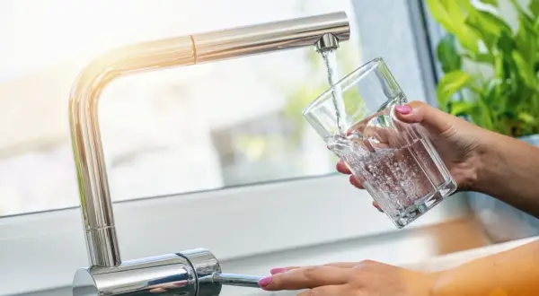Une main verse de l'eau fraîche du robinet dans un verre. Une idée simple pour comment refroidir de l'eau rapidement.