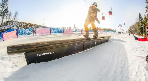 Snowboardzista na grindboxie w **Jaworzynie Krynickiej snowparku**. W tle kolejka linowa i inni narciarze.