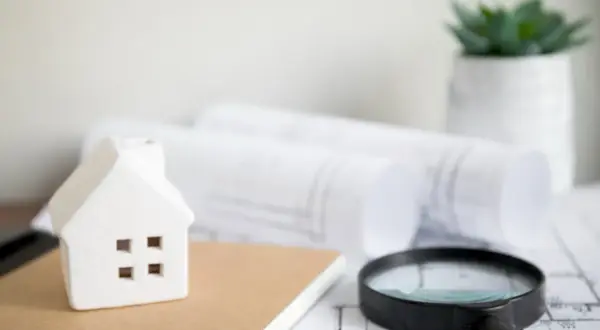 Modellino di casa, lente d'ingrandimento e progetti su un tavolo, pronti per un controllo edilizio.