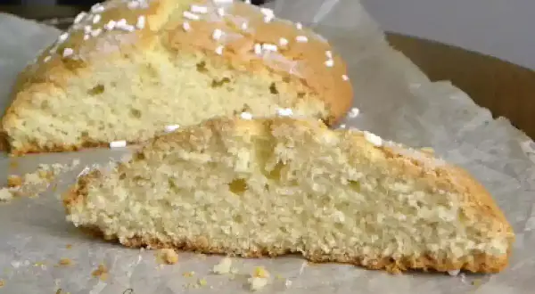 Fetta di ciambella romagnola soffice e dorata, cosparsa di zuccherini, su carta da forno.
