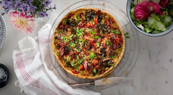 En gyllene quiche lorraine med broccoli, bacon och tomater, serverad med en fräsch sallad.