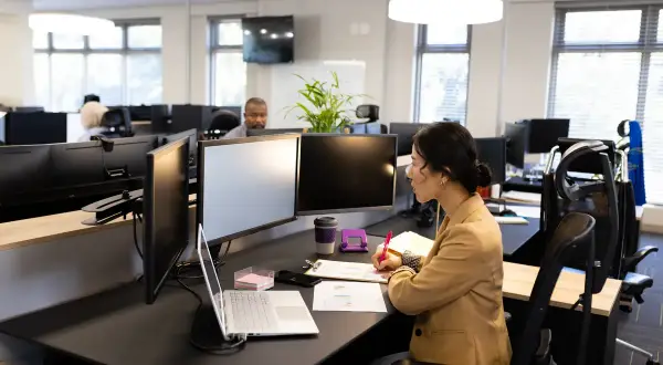 Une femme travaille à son bureau, entourée d'écrans. L'espace de travail semble bien organisé, suggérant une bonne gestion de la taille bureau m2.
