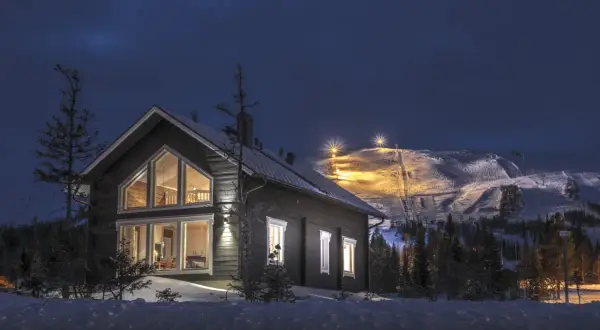 Trillevallen hotell, ett mysigt hus i snölandskap med upplysta skidbackar i bakgrunden.