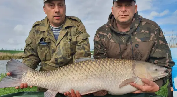 Dwóch wędkarzy prezentuje imponującego karpia o wadze 22 kg, złowionego na łowisku Nowe Żukowo.