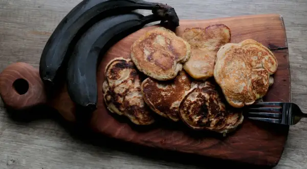 Placki bananowe z masłem orzechowym, obok ciemnych bananów, na drewnianej desce. Idealne na śniadanie.