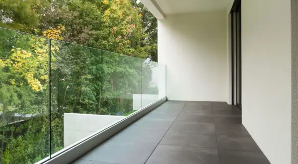 Nowoczesne płytki na balkon w bloku, z widokiem na zielony ogród i szklaną balustradę.