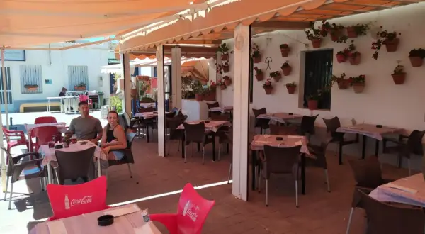 Pareja sonriente en la terraza de "La Chumbera Las Negras", un restaurante con mesas al aire libre y macetas de flores.