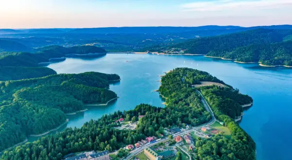 Widok z lotu ptaka na jezioro otoczone lasami, z widocznymi zabudowaniami i zaporą.