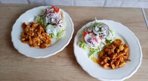 Dwa talerze z kurczakiem w przyprawach i sałatką z pomidorów, ogórków i cebuli. Tak wygląda pyszna shoarma co to za danie!