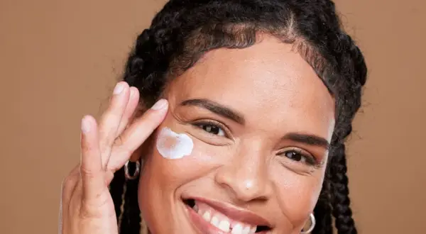 Lächelnde Frau trägt eine Creme auf, die für die vitamin c haut gedacht ist.