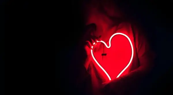 Een persoon houdt een gloeiend rood neonhart vast. Dit is wat ontgroend liefde kan voelen: warm, helder en vol passie.