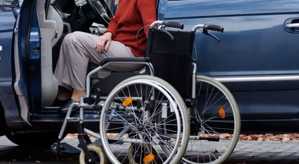 Osoba w wózku inwalidzkim obok otwartych drzwi samochodu. Ułatwia to wsiadanie i wysiadanie, zapewniając ulgę na samochód.