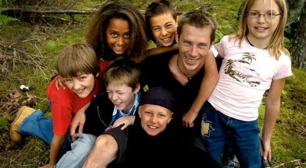 En grupp glada barn och en vuxen njuter av en dag i skogen. De ser ut som riktiga ola wild kids, redo för äventyr.