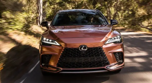 Miedziany Lexus RX 450h pędzi leśną drogą, światła LED rozświetlają trasę.