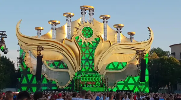 Złota, słoneczna scena festiwalowa z zielonymi światłami, gdzie jest sunrise, otoczona tłumem ludzi.