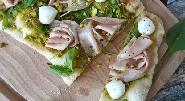 En läcker pinsa pesto med mortadella, mozzarella, pistagenötter och färsk basilika på en träskärbräda.