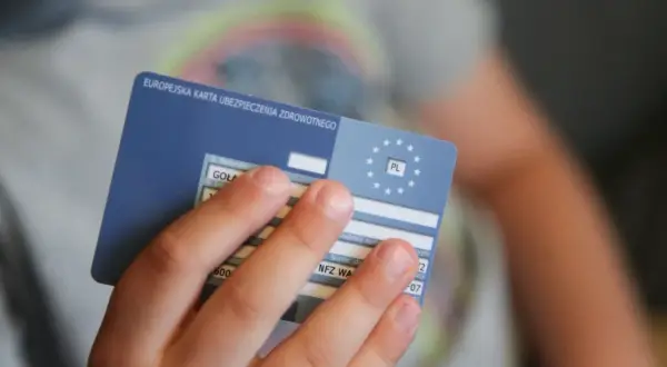 Dziecko trzyma Europejską Kartę Ubezpieczenia Zdrowotnego. To ważny dokument, gdy podróżujesz po Europie. Ekuz co to? To Twoje ubezpieczenie zdrowotne.