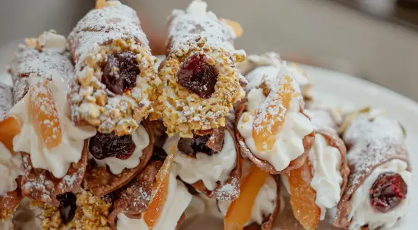 Cannoli garnis avec une généreuse crème de ricotta, des pistaches concassées, des cerises confites et des fruits confits. Saupoudrés de sucre glace.