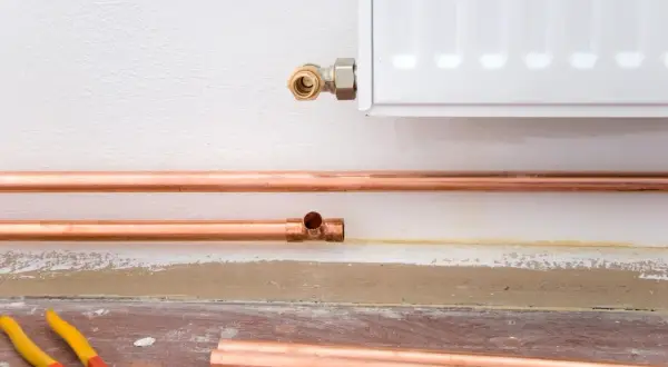 Installazione di tubi in rame per il riscaldamento, con un raccordo a T e una connessione al radiatore. La coibentazione dei tubi riscaldamento è fondamentale per l'efficienza.