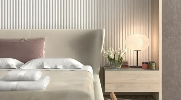 Elegancka sypialnia z łóżkiem, na którym leżą białe ręczniki i różowa poduszka. Ściana za łóżkiem ozdobiona jest pionowymi **lamele w sypialni**.
