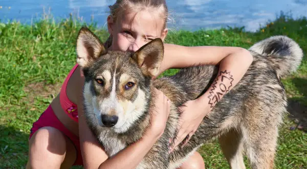 Dziewczynka mocno przytula swojego ukochanego psa kundla. Na jej ramieniu widnieje napis "LOVE".