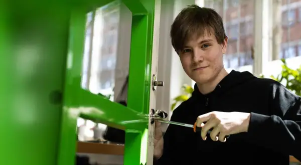 En ung man skruvar i ett dörrhandtag, en praktisk övning på Praktiska Gymnasiet Gamlestaden.