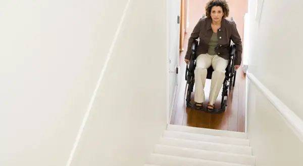 Donna in carrozzina guarda verso l'alto, pronta per il trasporto disabile su per le scale.