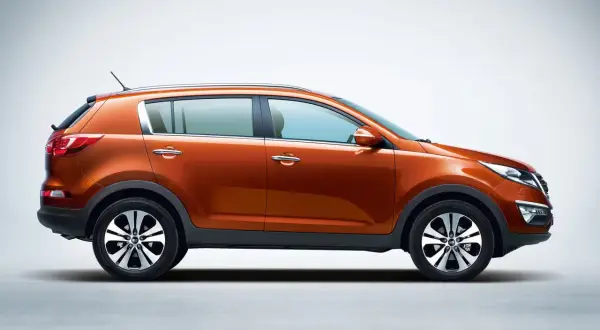 Pomarańczowy Kia Sportage 2013 z profilu, z błyszczącymi felgami i chromowanymi klamkami, gotowy na przygodę.