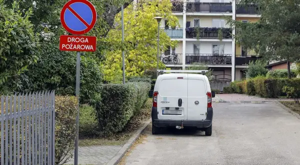 Znak "zakaz zatrzymywania się" i "droga pożarowa" obok białego vana. Kierowca może spodziewać się mandatu za złe parkowanie od straży miejskiej.